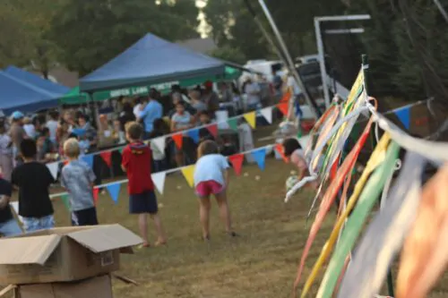 Festival extérieur avec des enfants qui jouent autour de banderoles triangulaires accrochées. chapiteaux au loin et gens qui circulent sur le site