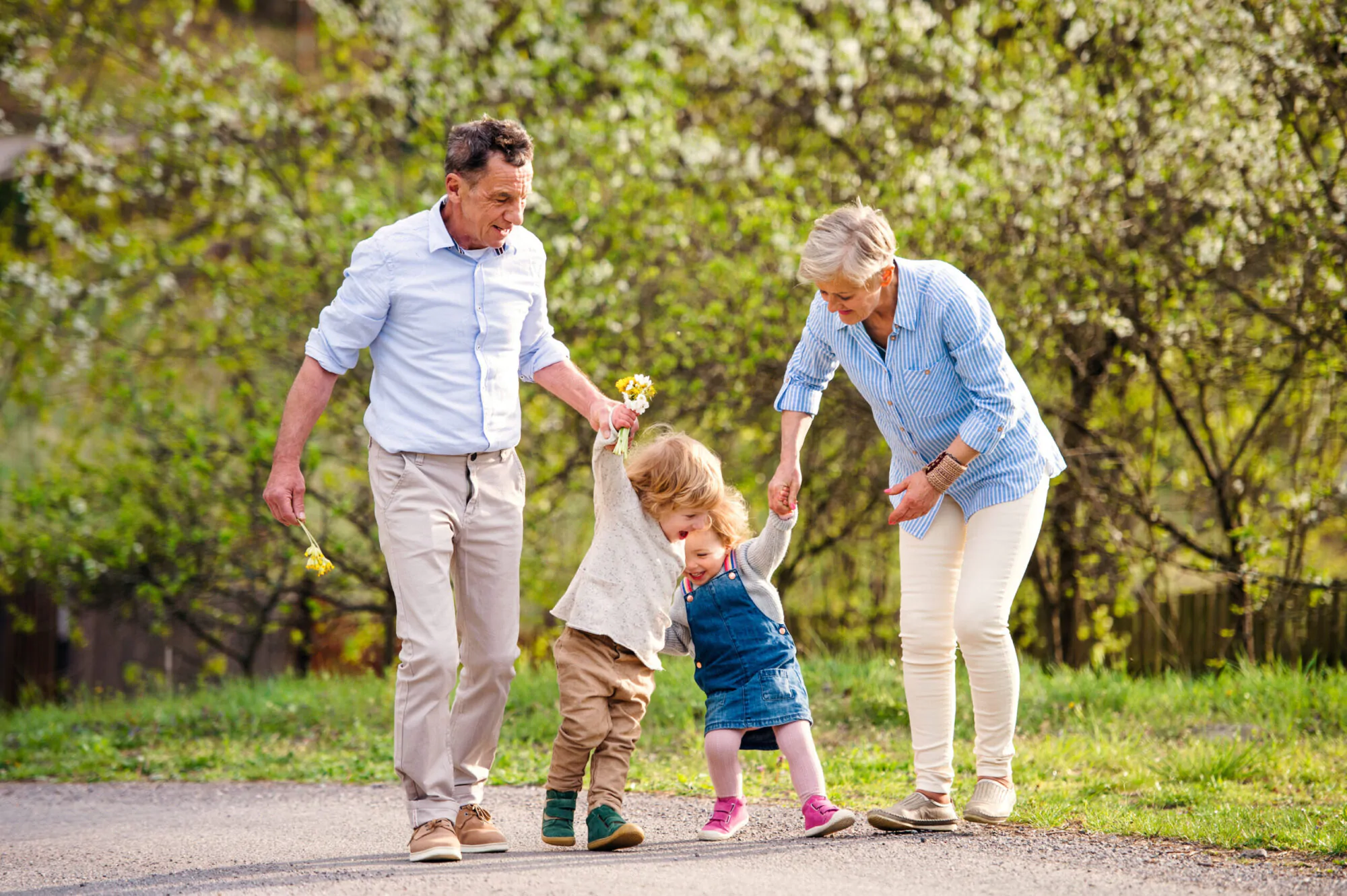 Des grands-parents marchent avec des enfants sur un sentier avec des arbres en fleur derrière eux.
