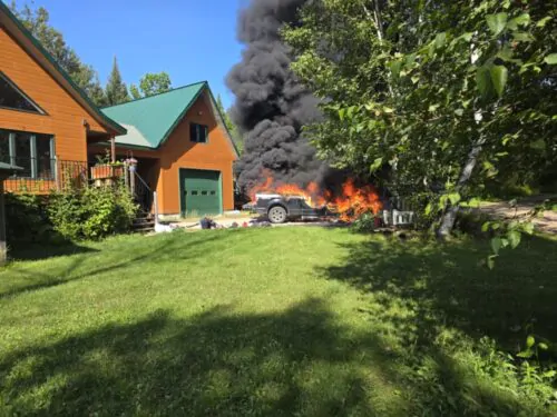 Des flammes s'échappent d'un véhicule en flamme devant une résidence de campagne.