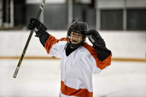 enfant, joueur d'hockey sur patinoire intérieure avec équipement d'hockey complet, casque noir, gants noirs et chandail d'hockey blanc et orange, célébrant la victoire