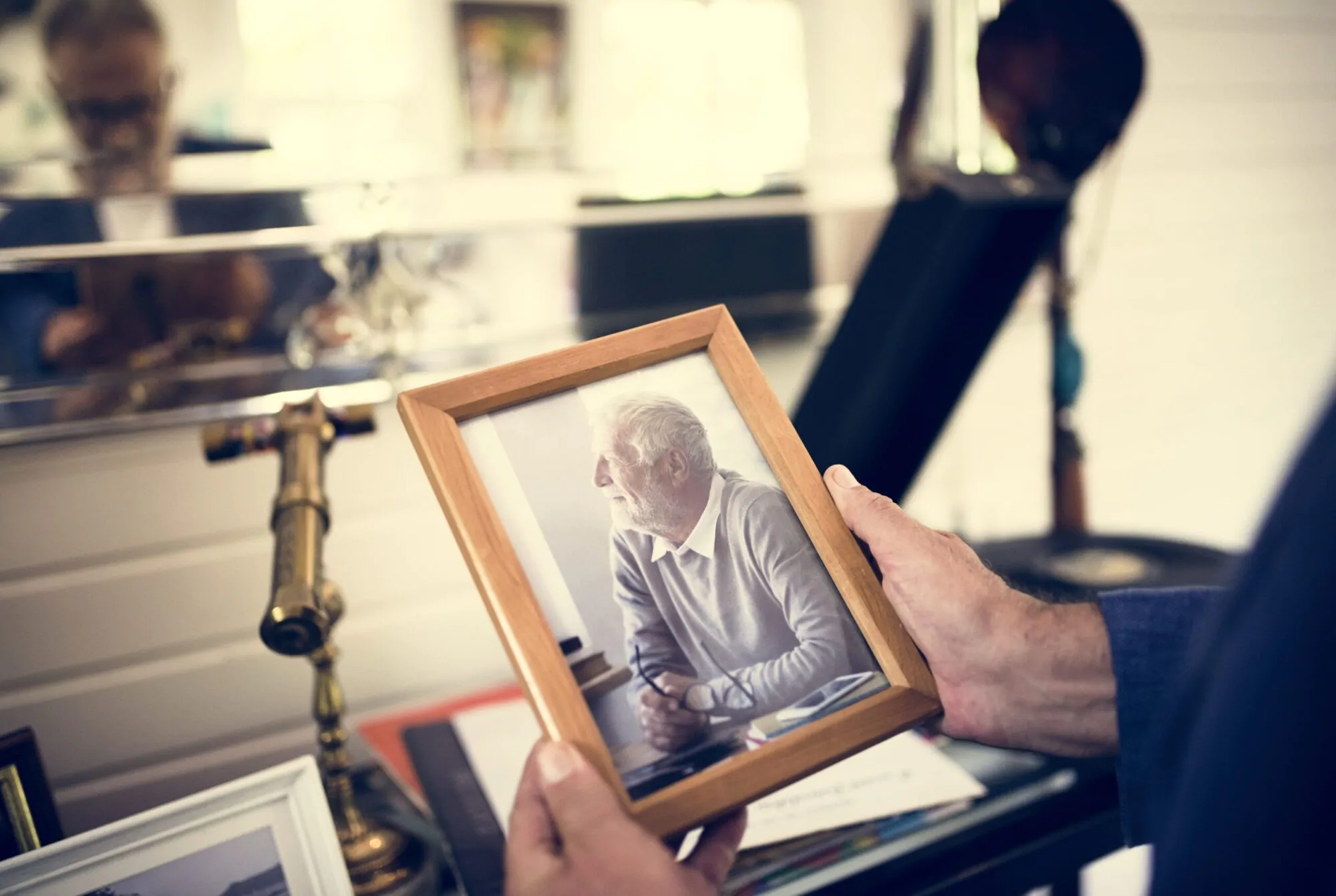 Une personne tient un cadre photo représentant un homme âgé avec en arrière-plan un intérieur de maison contenant des objets du quotidient.