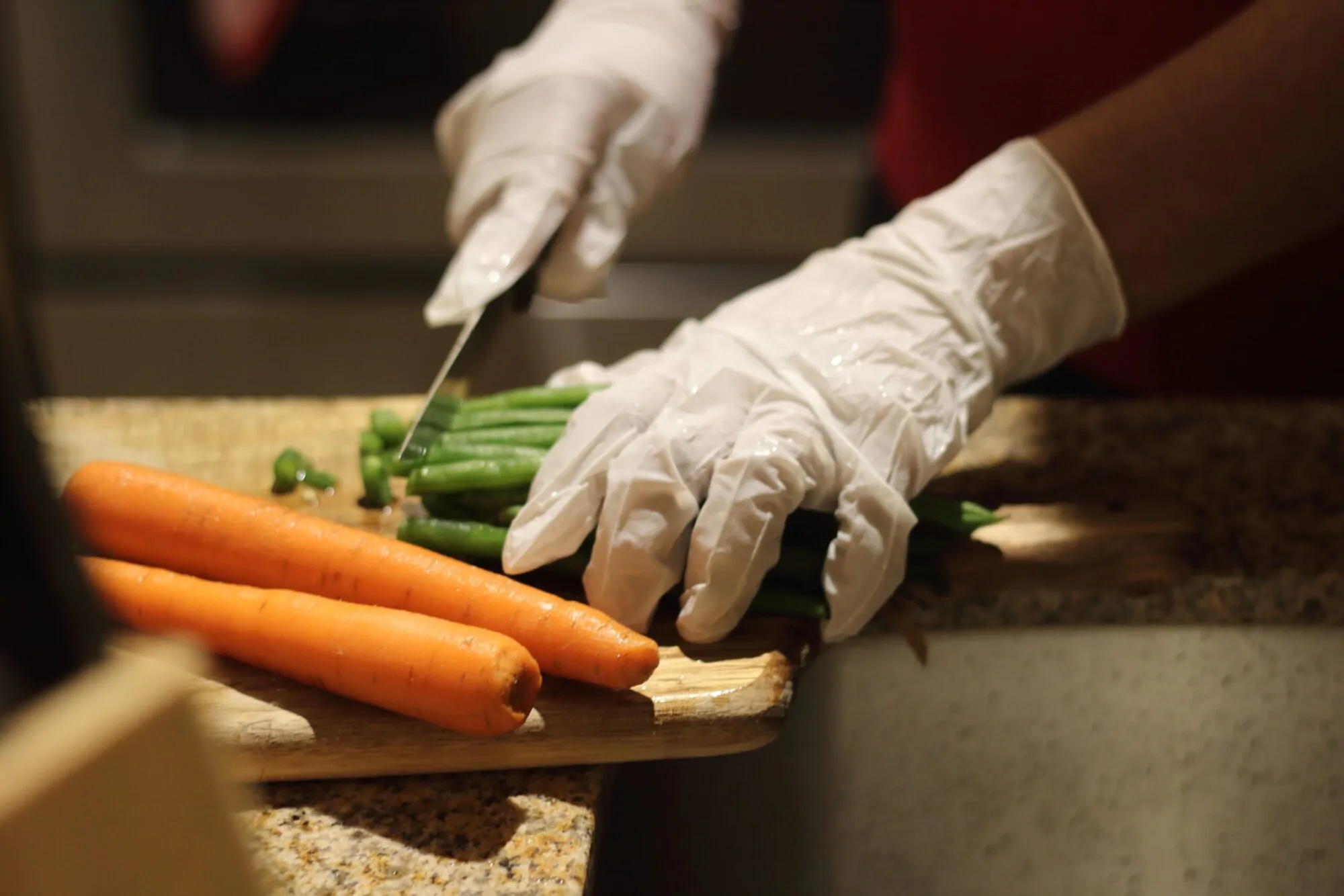 Une personne découpe des carottes et des haricots verts sur une planche en bois.