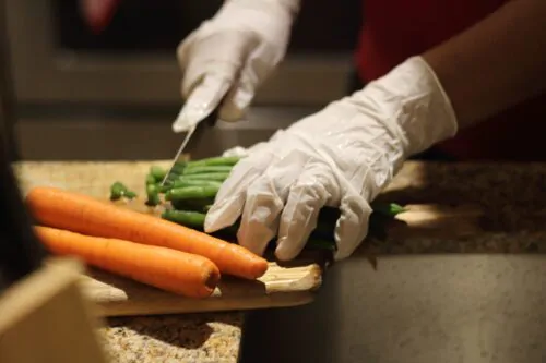 Une personne découpe des carottes et des haricots verts sur une planche en bois.