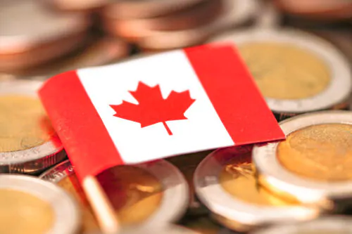 Un petit drapeau de papier canadien posé sur une pile de pièces de deux dollars.