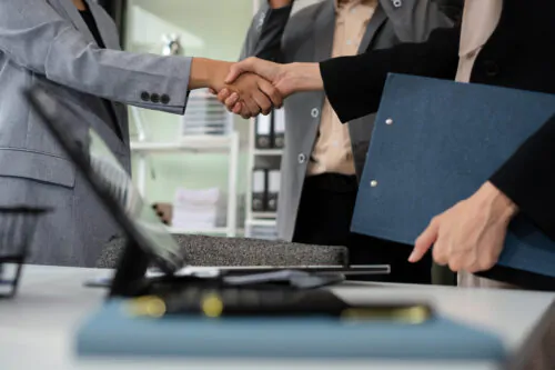 Happy businessman and businesswoman shaking hands at group board