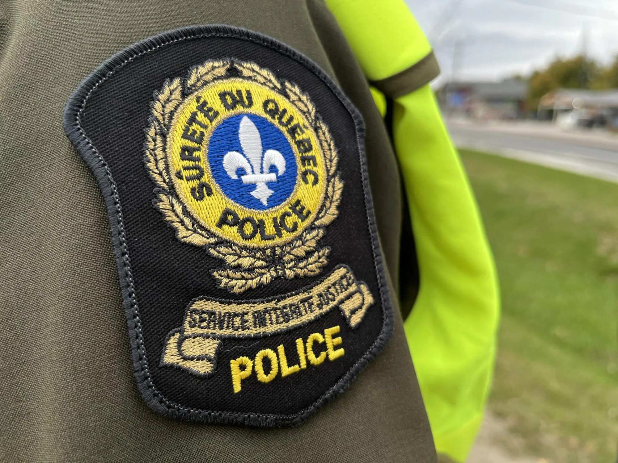 Un écusson de la Sûreté du Québec sur la manche d'un policier posté près d'une route.