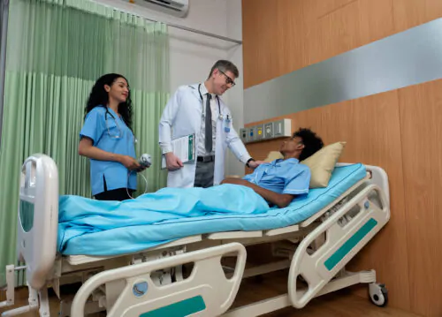 Une infirmière et un médecin s'adressent à une patiente allongée dans une chambre d'hôpital.