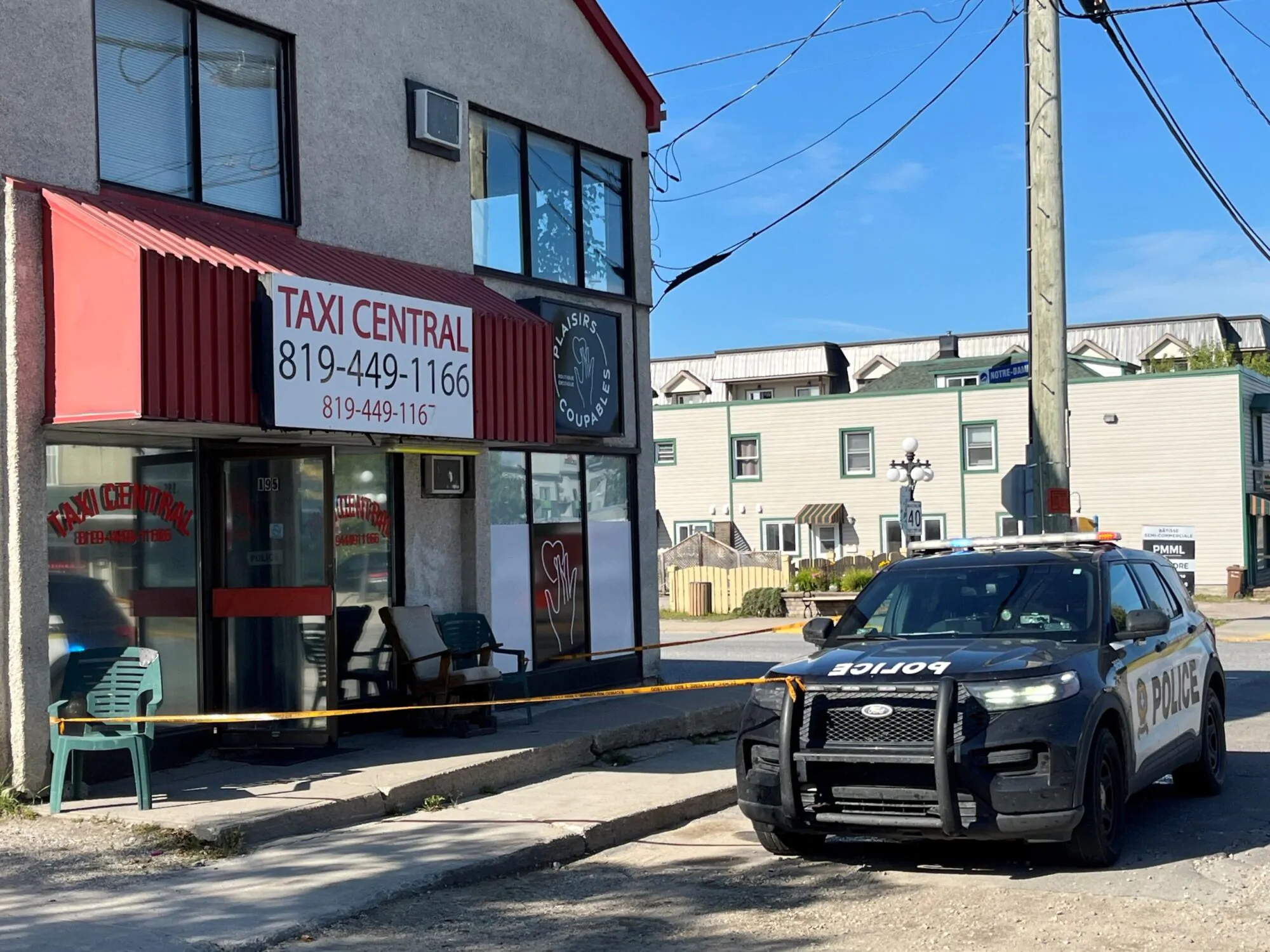 Un commerce de taxi à Maniwaki devant lequel une voiture de police est stationnée. Un ruban jaune de sécurité entoure l’entrée, indiquant une intervention ou une enquête policière en cours.