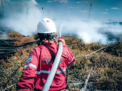 Un pompier forestier de la SOPFEU, vu de dos, éteint un incendie à l'aide d'une hausse.