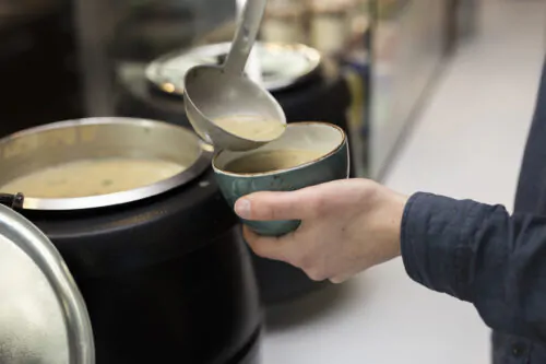 A person serving hot soup into a bowl from a tureen