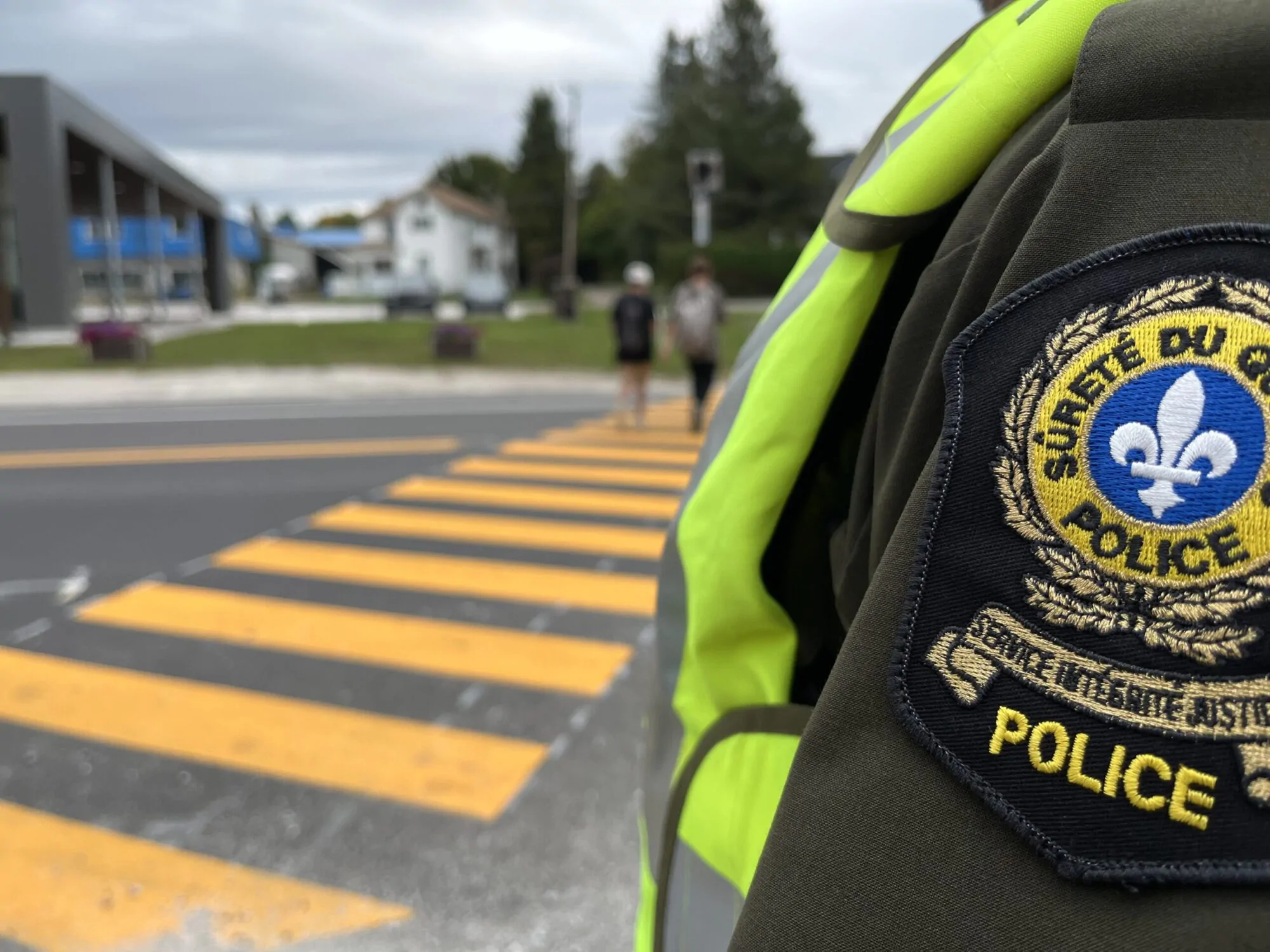 Un policier de la Sûreté du Québec à proximité d'un passage piéton sur lequel deux personnes marchent.