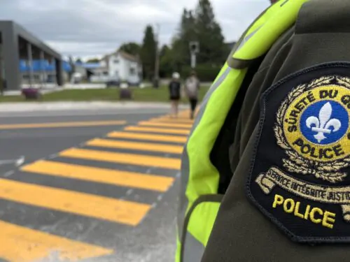 Un policier de la Sûreté du Québec à proximité d'un passage piéton sur lequel deux personnes marchent.