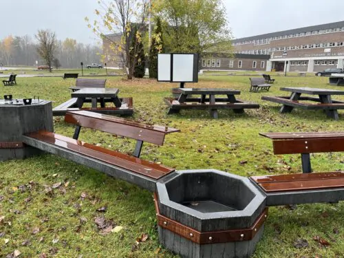 Des tables de pique-nique, des bancs, des ports à fleurs et un tableau sur le terrain d'une école.