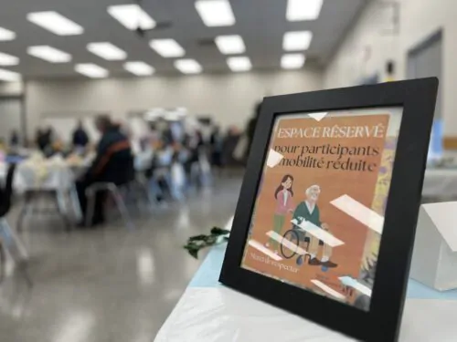 Un cadre montrant une personne aînées en chaise roulante est posée sur une table lors d'un événement dans une salle.