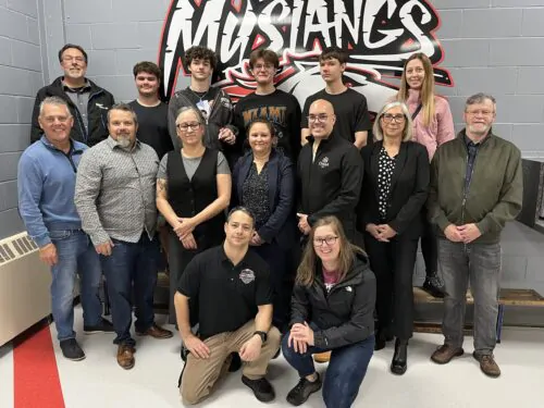 Un groupe de personne prend la pose sous le logo de l'équipe des Mustangs.