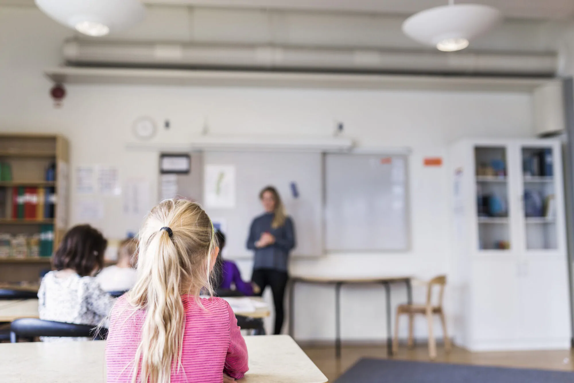 Des élèves d'âge primaire écoutent une enseignante dans une salle de classe.