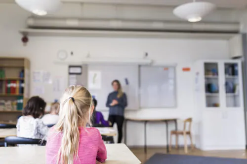 Des élèves d'âge primaire écoutent une enseignante dans une salle de classe.