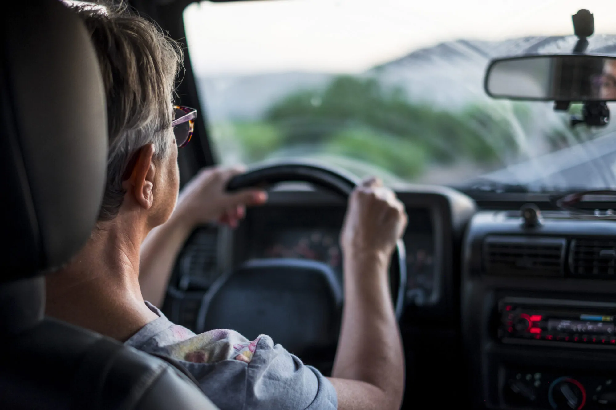 Une aînée vue de dos conduit une voiture en ayant les deux mains sur le volant.