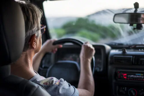 Une aînée vue de dos conduit une voiture en ayant les deux mains sur le volant.