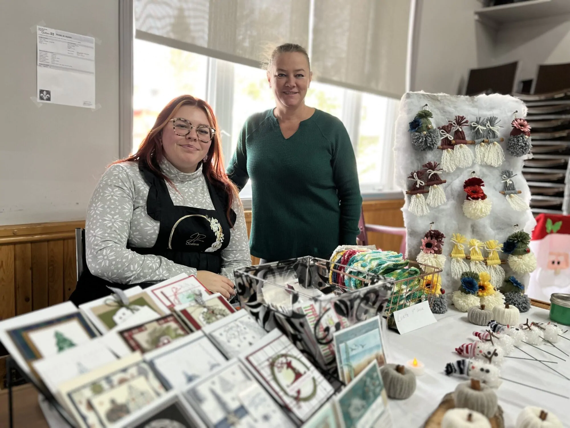 Deux femmes prennent la pose derrière une table garnie de produits artisanaux lors d'une foire de Noël .