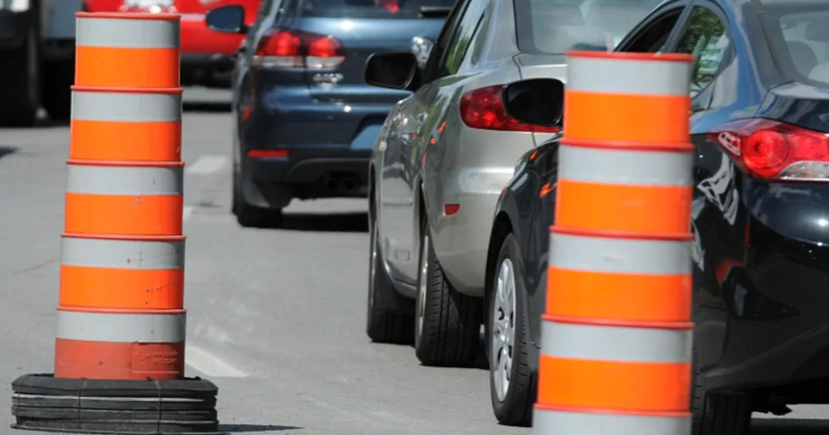 Des voitures font la file près d'un cône orange de chantier routier.