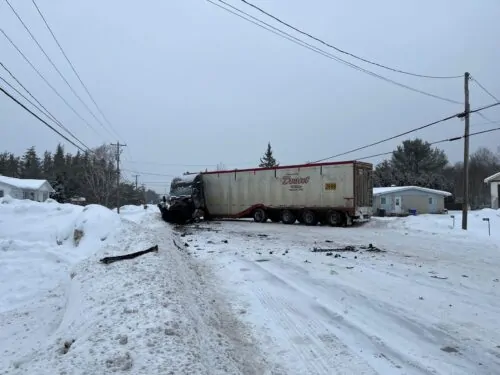 un camion semi-remorque est accidenté en travers de la chaussée, bloquant complètement la route enneigée.