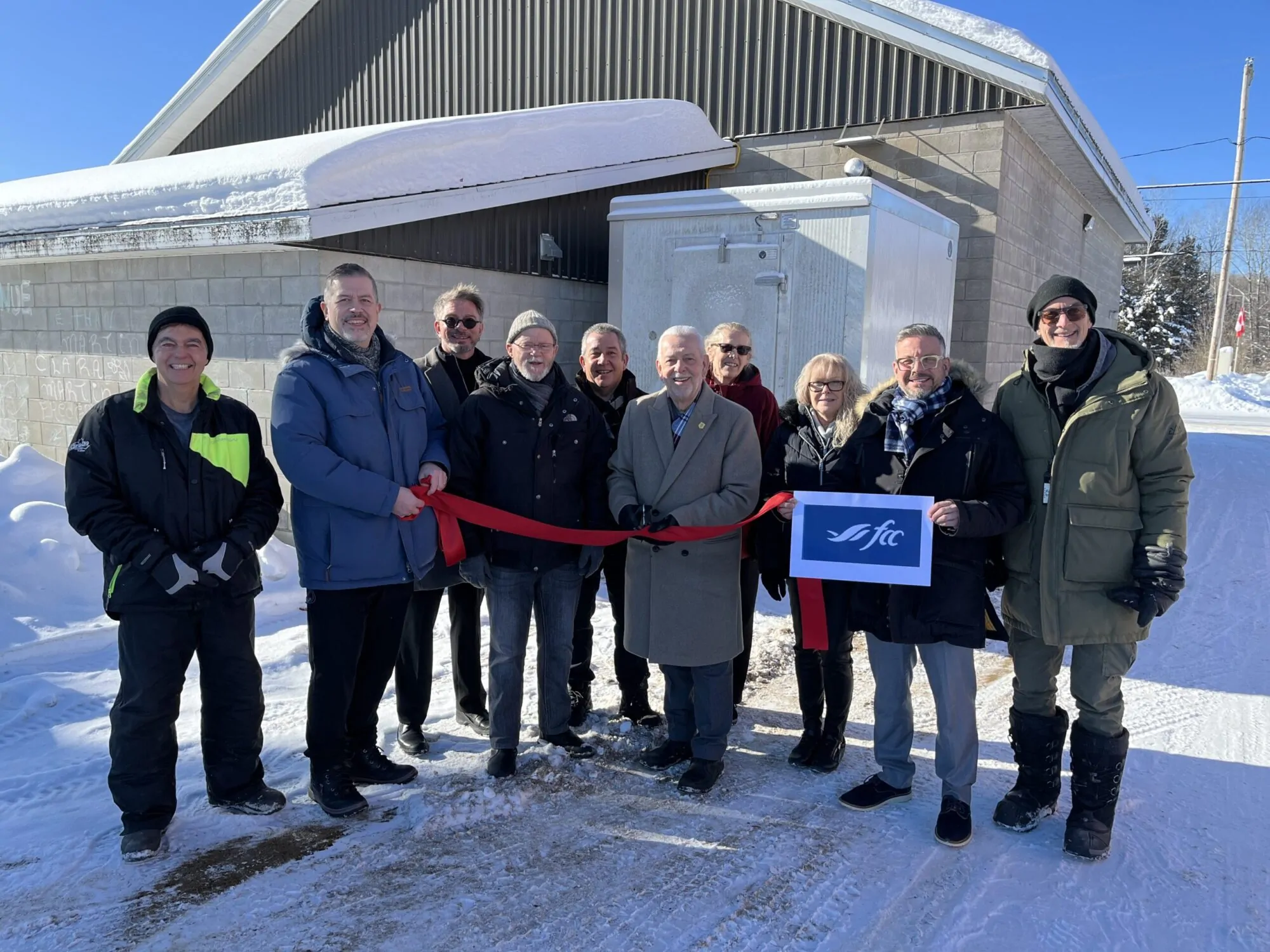 Un groupe de personnes procède à une coupure de ruban protocolaire près d'un bâtiment en hiver.