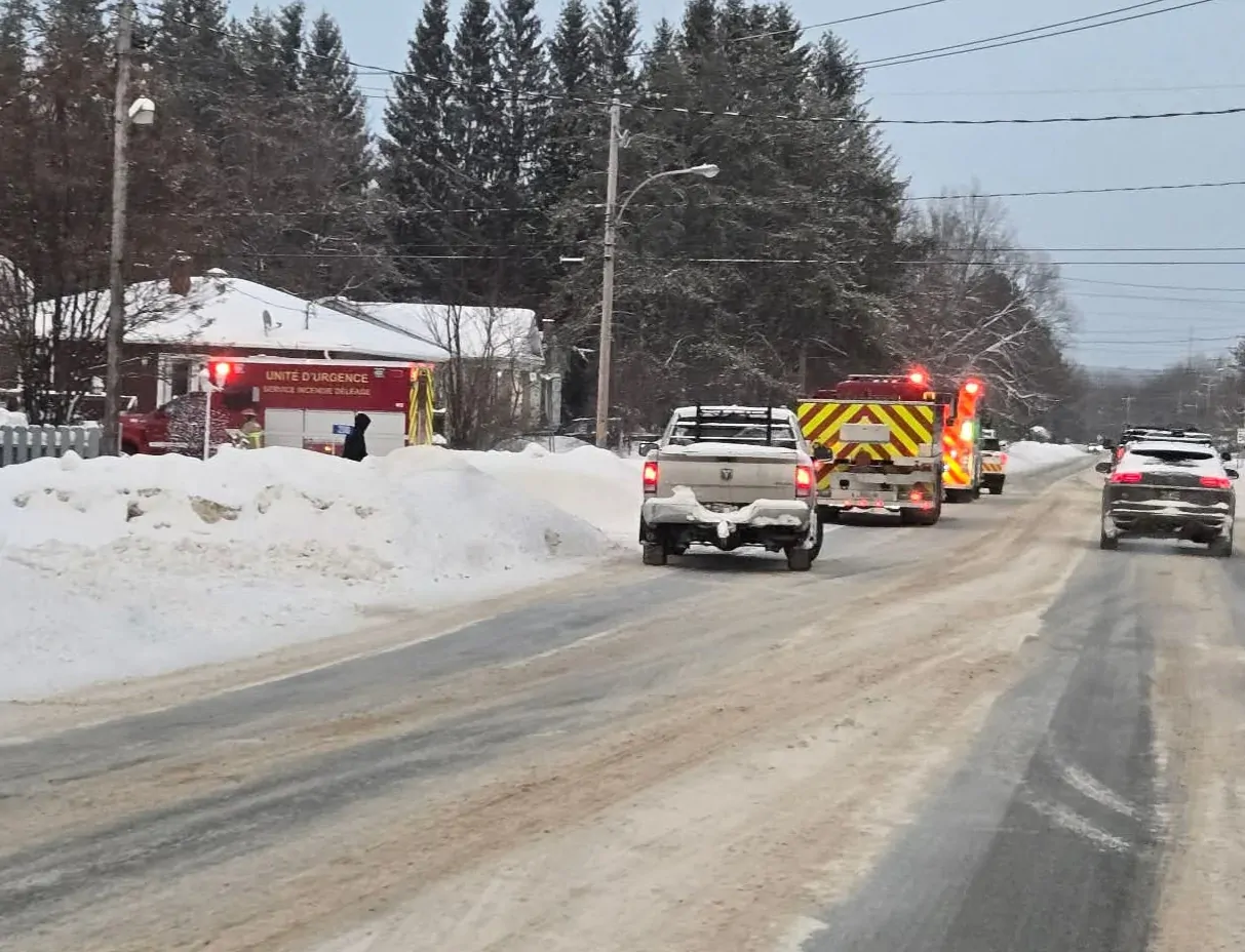 Des véhicules de pompiers sont stationnés en bordure de route, près de maisons, en hiver.
