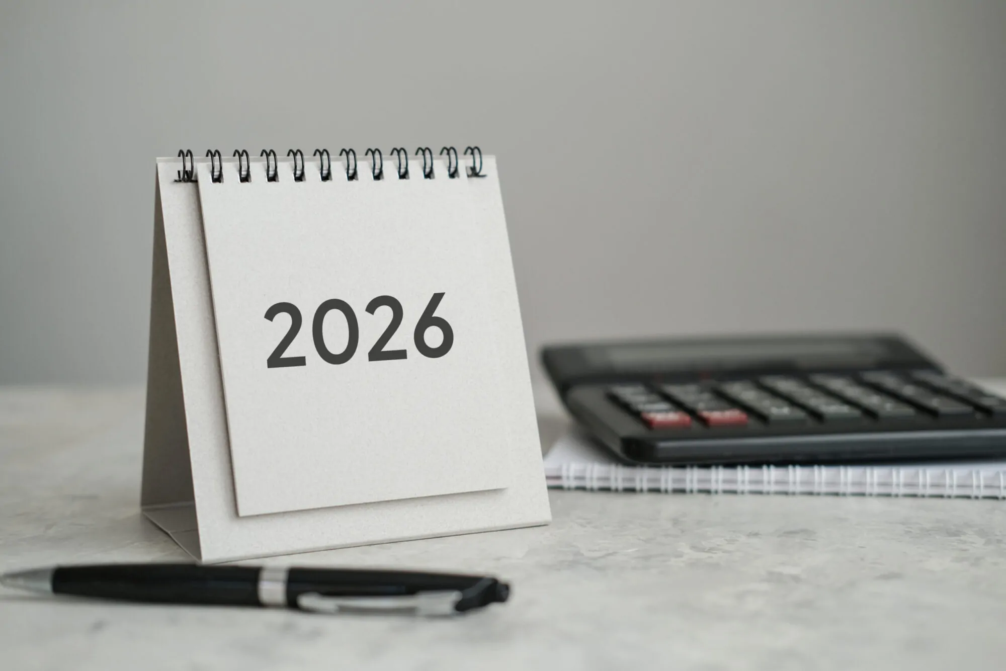 Desk calendar displaying year 2026, alongside calculator and pen. Perfect for showcasing concepts of finance, accounting, planning and business