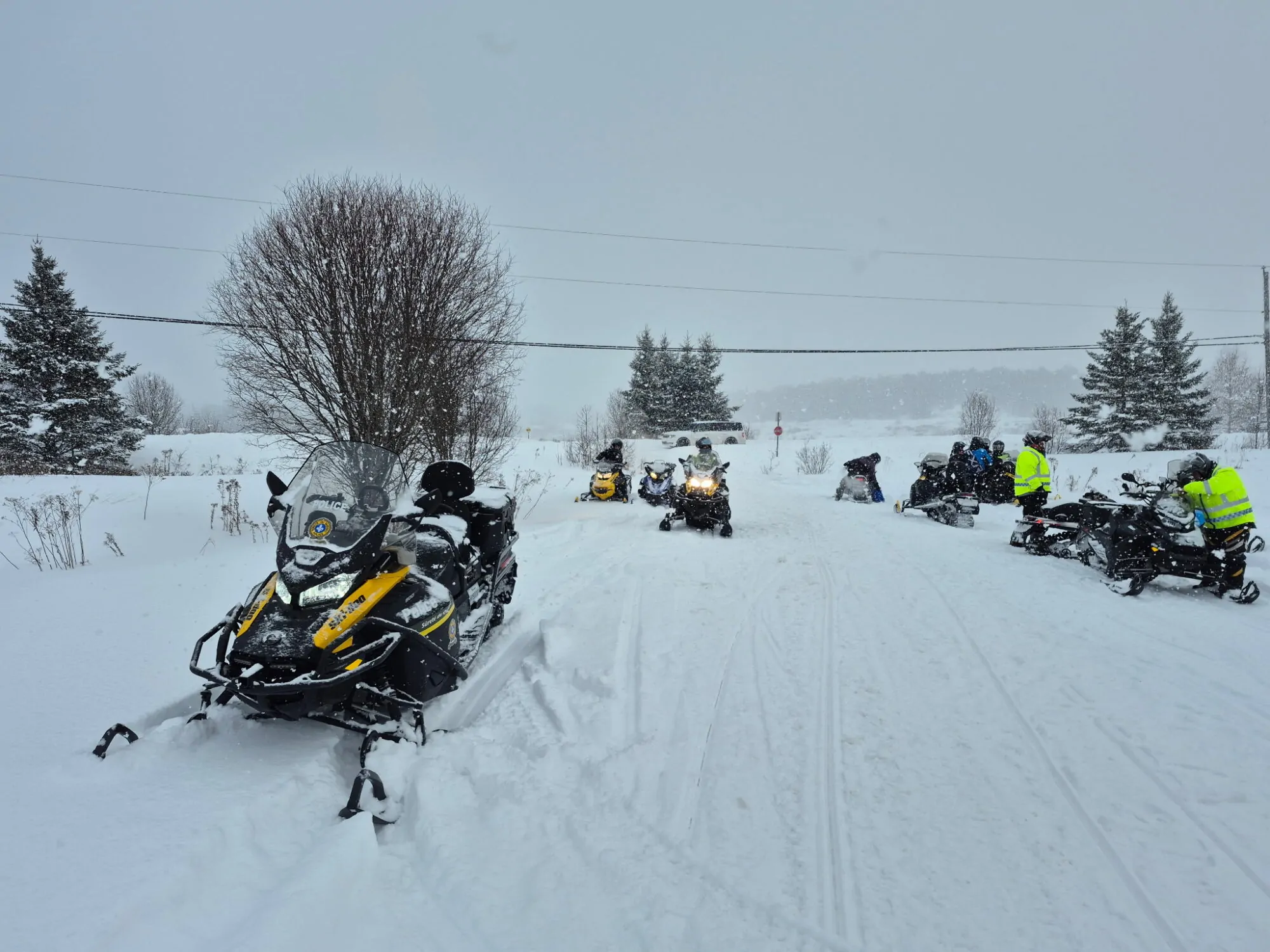 Des patrouilleurs de la Sûreté du Québec contrôlent des motoneigistes sur un sentier en plein hiver.